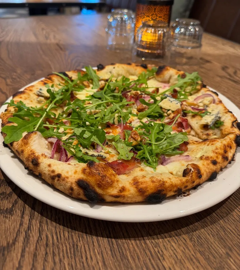 Pizza med ruccola, rødløk og blåmuggost på bordet hos Erica mat & vinbar